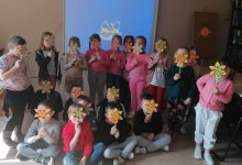 dzieci stoją na środku sali i prezentują wykonane samodzielnie kwiaty kolorowego papieru