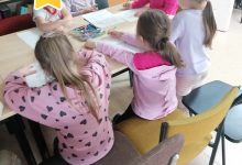 Dzieci siedzą przy stolikach i tworzą prace plastyczne kolorując radosne drzewo i smutne drzewo.
