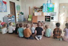 Dzieci siedzą na dywanie w sali przedszkolnej, nauczycielka czyta bajkę teatru kamishibai
