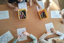 Dzieci siedzą przy stoliku i wykonują kolorowanki myszki