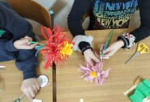 Dzieci wykonują przy stoliku kwiaty z papieru