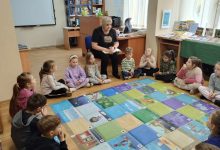 Na podłodze leży mata edukacyjna, dookoła siedzą dzieci. Nauczycielka czyta dzieciom opowiadanie.