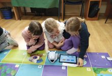 Trzy dziewczynki wyznaczają na ekranie tabletu drogę dla robota.