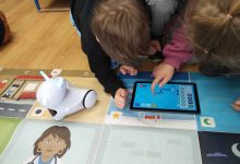 Na macie stoi robot Photon EDU. Dziewczynka i chłopiec pochyleni nad tabletem kodują robota.
