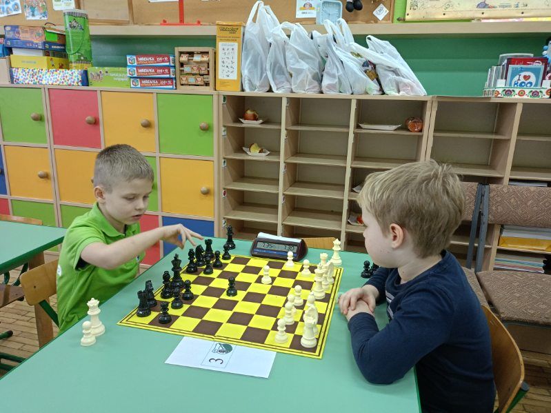 dzieci siedzą przy stoliku i grają w szachy