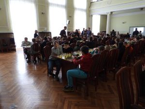 Dzieci siedzą za stołami, na których są szachownice.